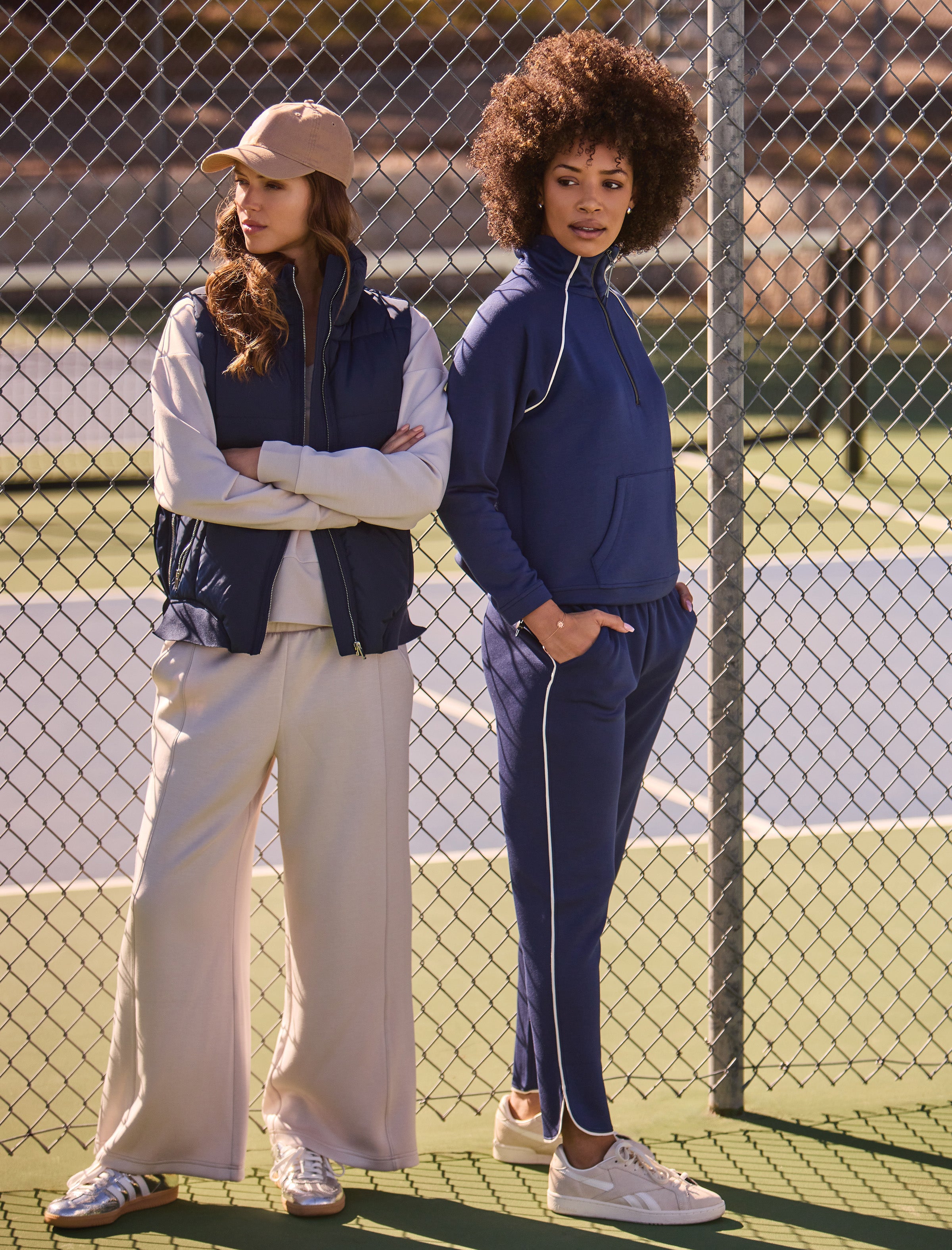 Two women standing on a tennis court wearing casual outfits.