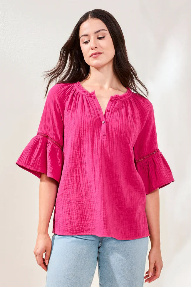 Woman wearing a bright pink blouse with ruffled sleeves against a plain background