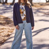 Woman standing outdoors wearing a navy cardigan, floral blouse, and light blue jeans.