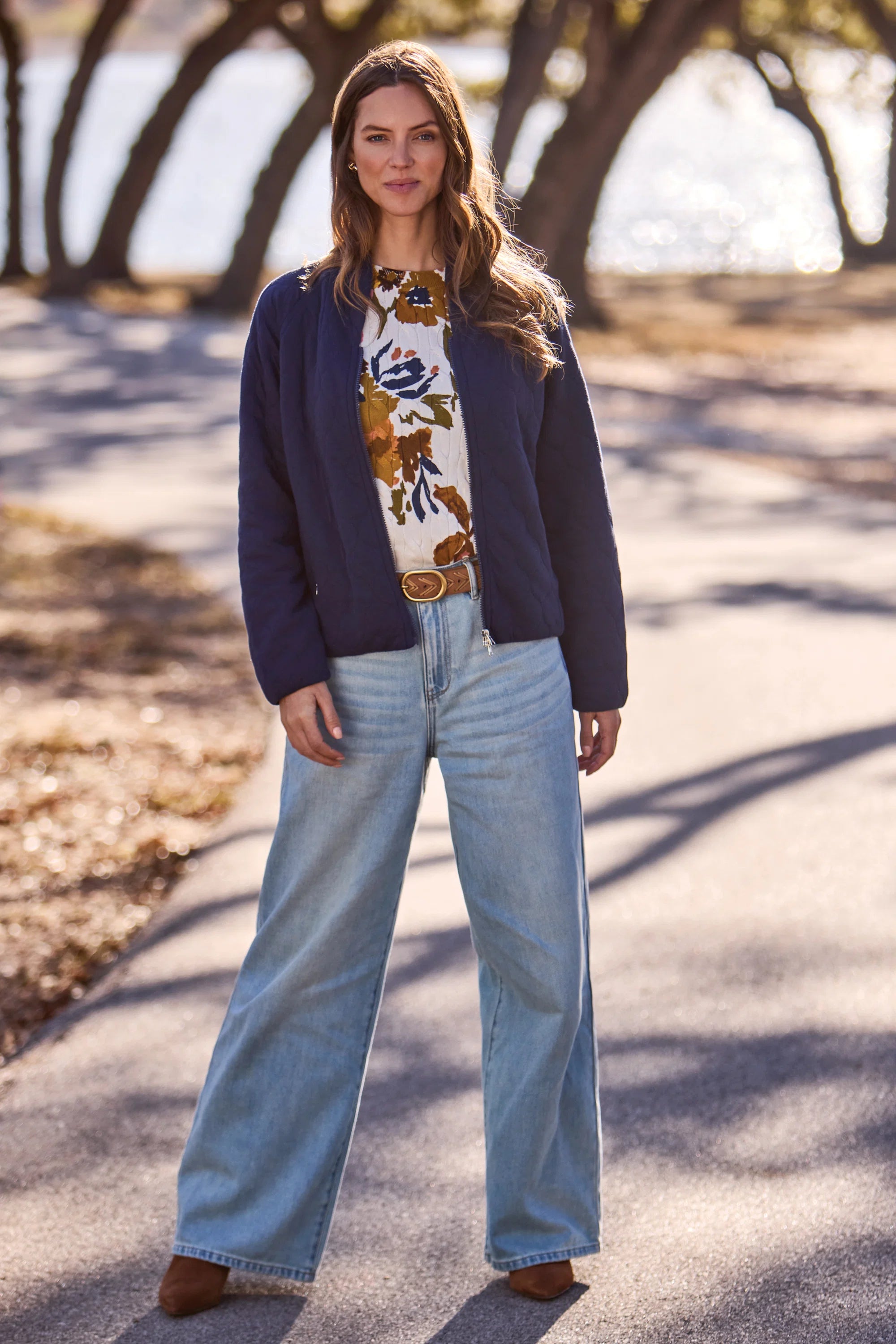 Woman standing outdoors wearing a navy cardigan, floral blouse, and light blue jeans.