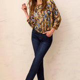 Woman wearing a patterned blouse and jeans against a light background