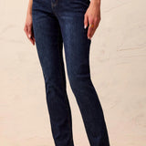 Person wearing dark blue jeans and a patterned top on a light wooden floor.