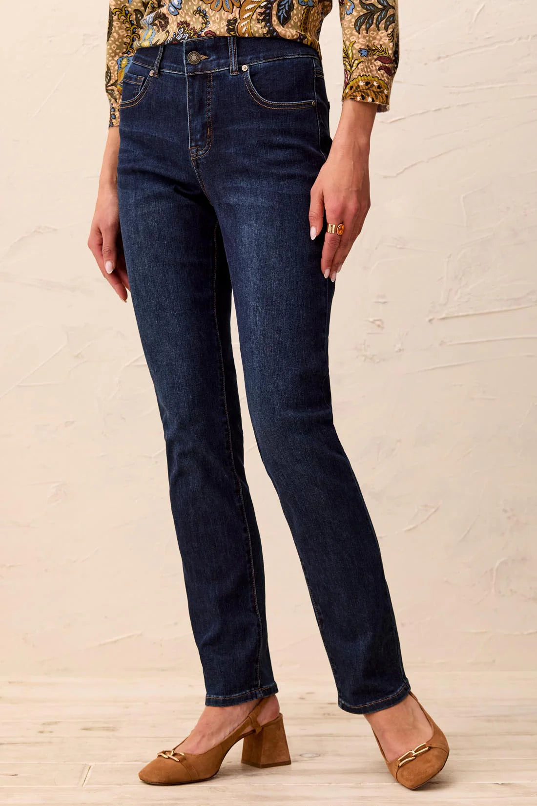 Person wearing dark blue jeans and a patterned top on a light wooden floor.