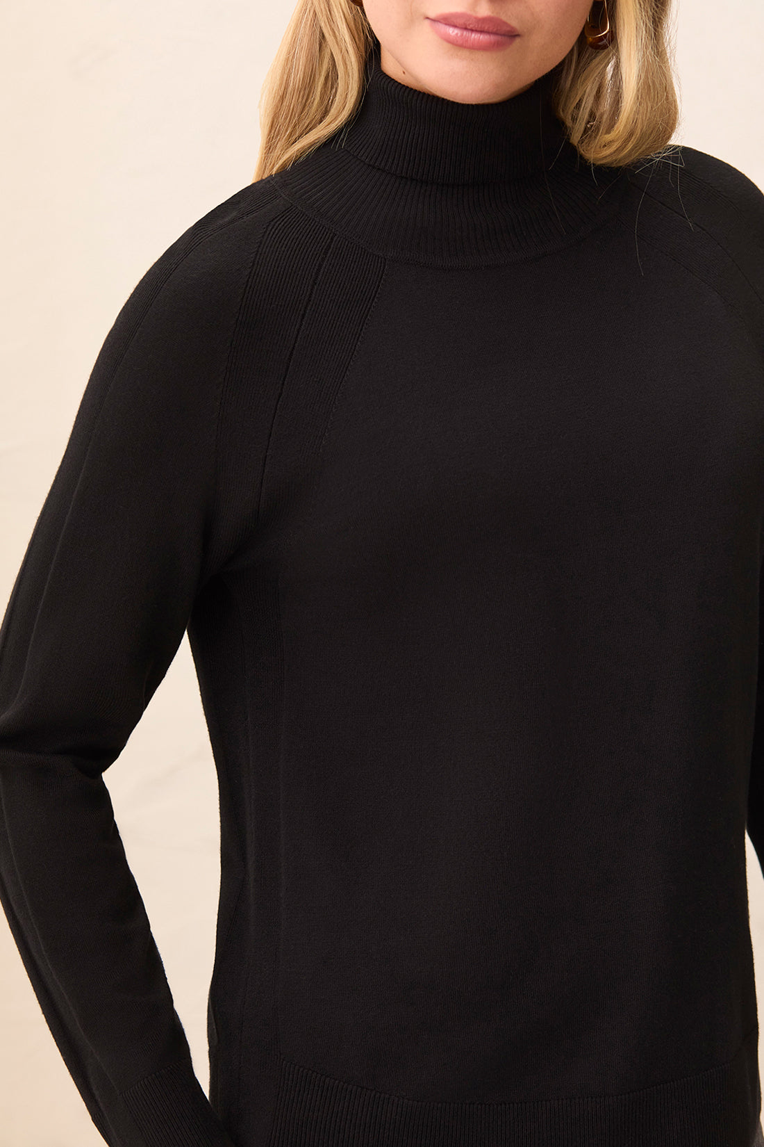 Black turtleneck sweater worn by a person on a beige background