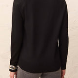 Person wearing a black long-sleeve top with a textured white wall background