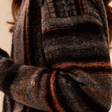 Close-up of a textured knit sweater with horizontal stripes in charcoal gray, black, and rust orange, worn by a model.