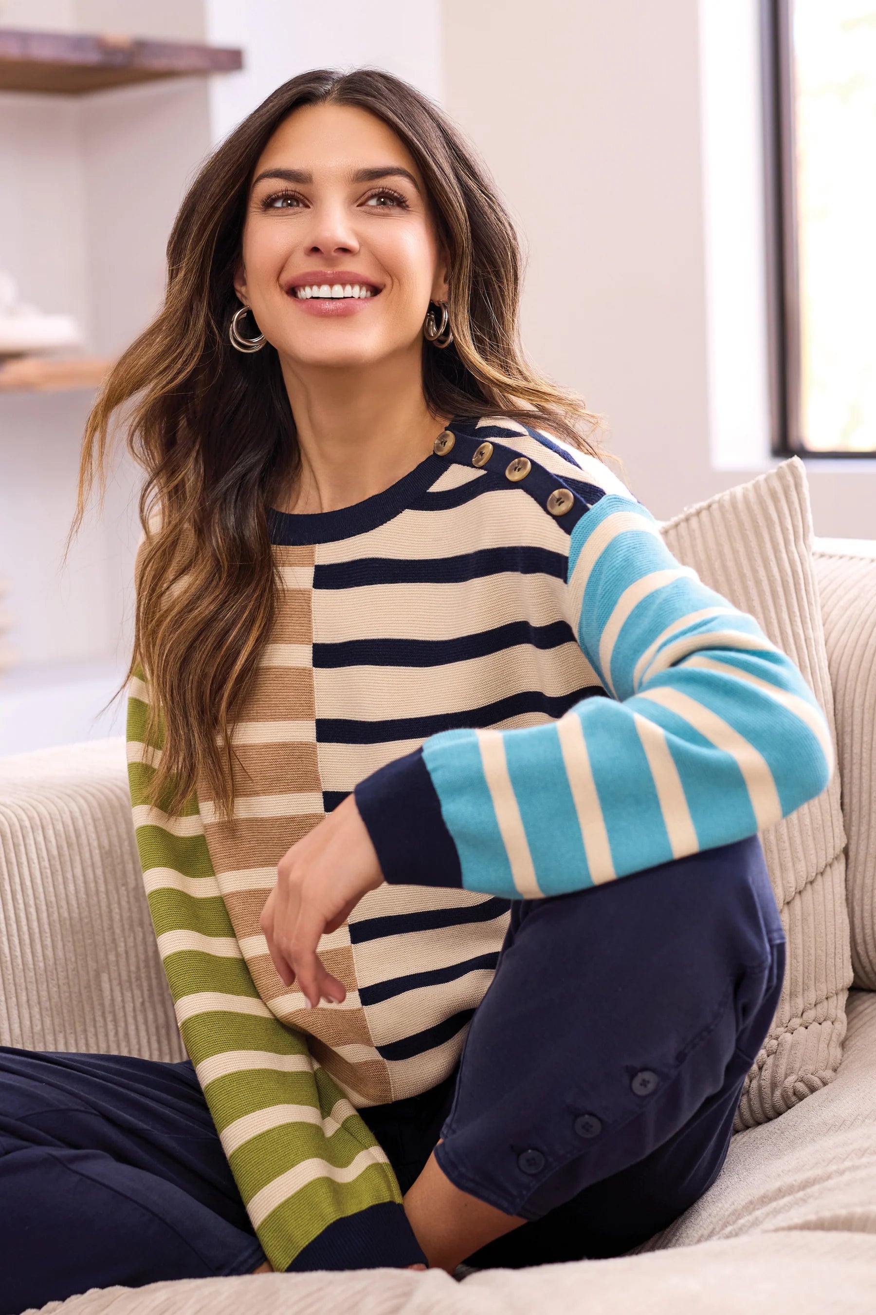 Woman wearing a striped sweater sitting on a couch in a bright room.