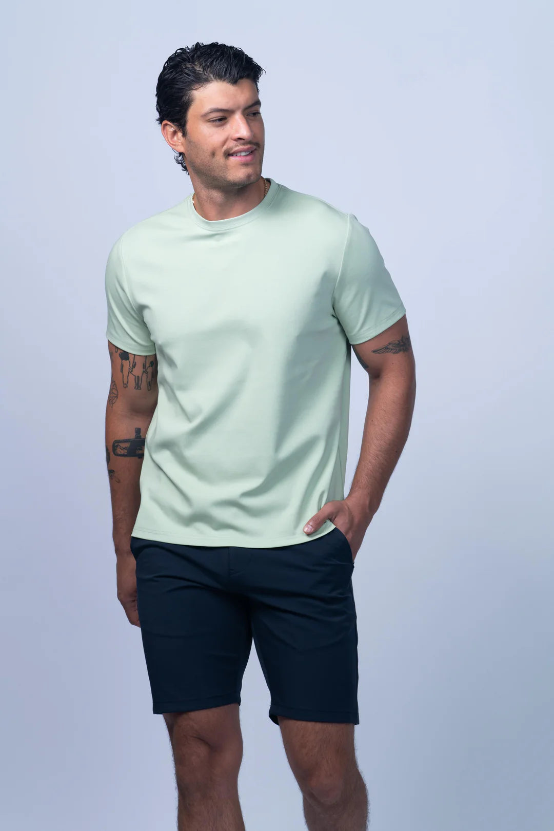 Man wearing a light green t-shirt and navy shorts on a light gray background