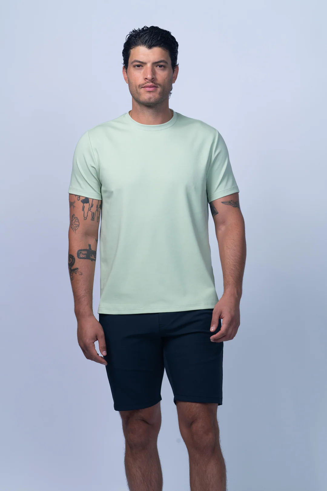 Man wearing a light green t-shirt and navy shorts on a plain background