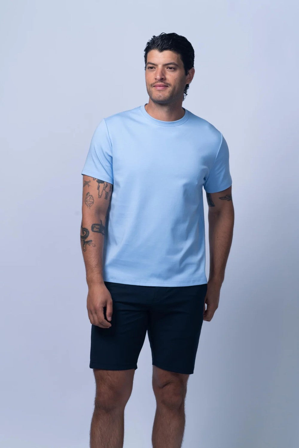 Man wearing a light blue t-shirt and dark shorts on a light gray background