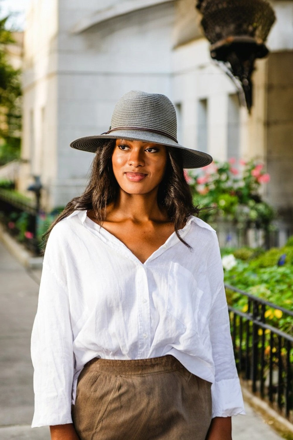 Woman wearing a white shirt and brown pants with a gray hat in an urban setting.