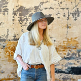 Woman wearing a white blouse, blue jeans, and a gray hat against a textured wall.