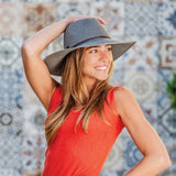 Woman wearing a red dress and gray hat against a patterned wall.