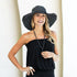 Woman wearing a black strapless top and wide-brimmed hat against a white background