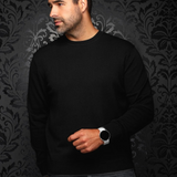 Man wearing a black Au Noir LACAUNE cashmere sweater from Broderick's Clothing Co. against a dark patterned wall.