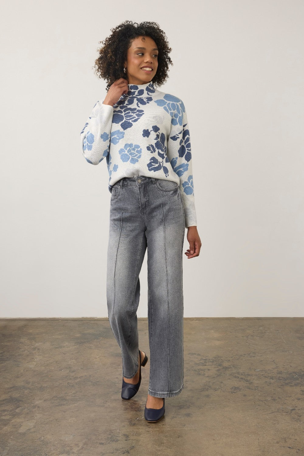 Broderick's Clothing Co. model wearing blue-gray wide-leg jeans with pintuck detail and a floral mock-neck sweater.