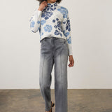 Broderick's Clothing Co. model wearing blue-gray wide-leg jeans with pintuck detail and a floral mock-neck sweater.