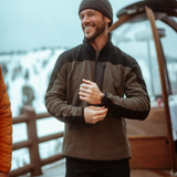 Broderick's Clothing Co. KÜHL SKORCHR fleece quarter-zip sweater in olive and black worn by a man in a snowy setting.