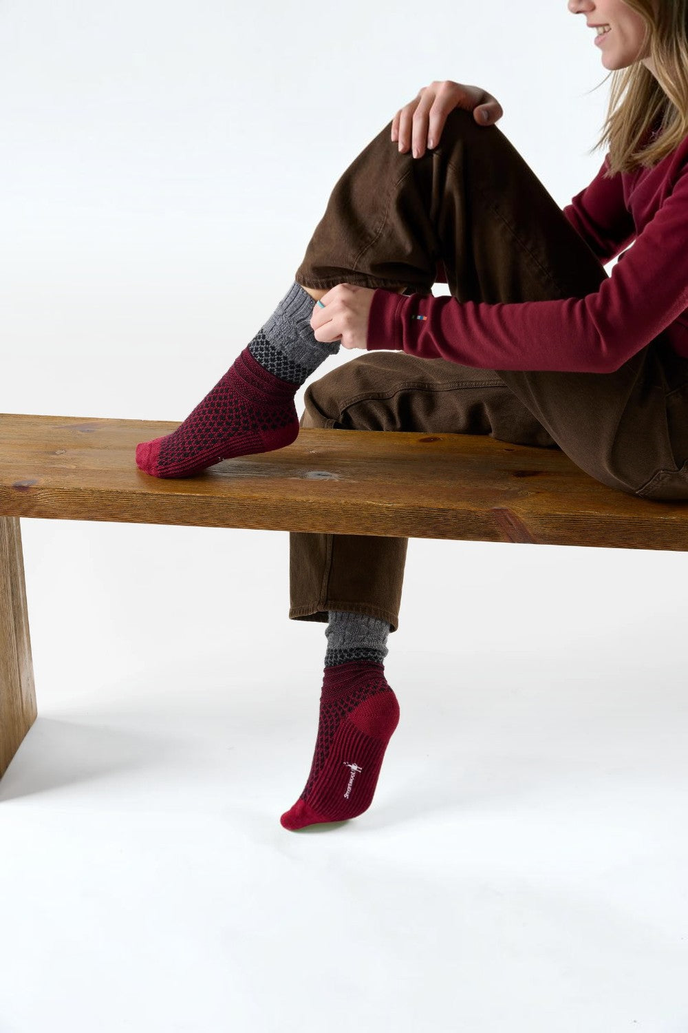 Broderick's Clothing Co. Smartwool women's burgundy popcorn cable crew socks with grey cuffs worn by a seated woman.