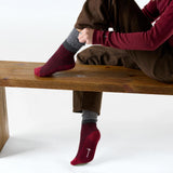 Broderick's Clothing Co. Smartwool women's burgundy popcorn cable crew socks with grey cuffs worn by a seated woman.