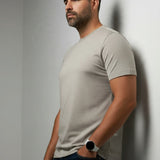 Broderick's Clothing Co. Au Noir C-MAVEN beige modal and mercerized cotton t-shirt worn by a man against a wall.