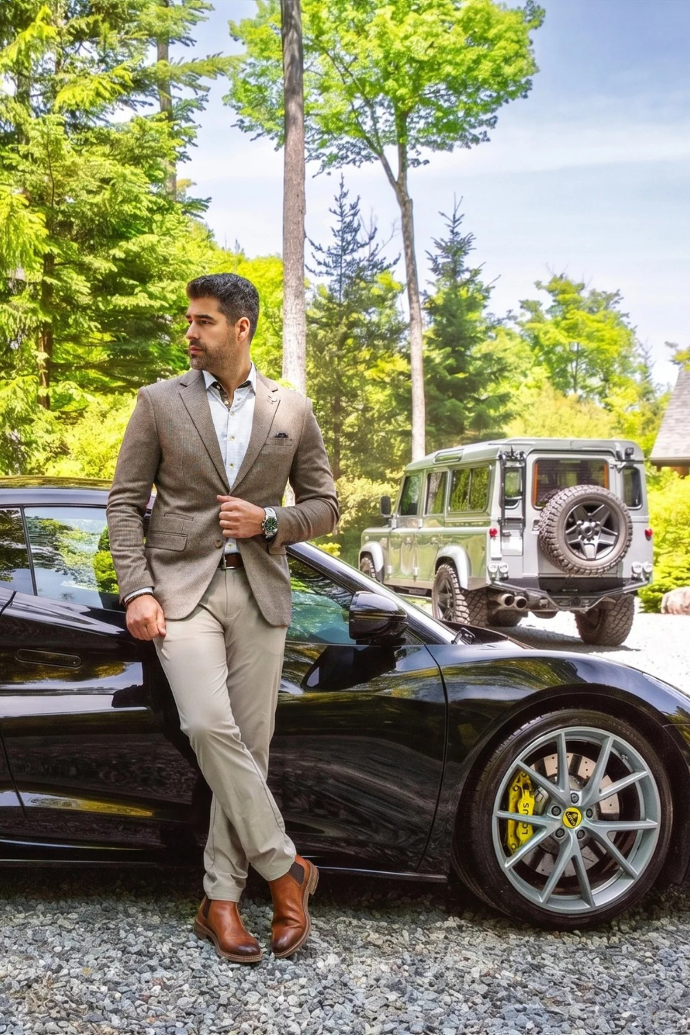 Man wearing a Broderick's Clothing Co. Au Noir EAMES brown blazer, white shirt, and beige trousers by a black sports car.