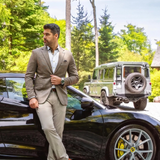 Man wearing a Broderick's Clothing Co. Au Noir EAMES brown blazer, white shirt, and beige trousers by a black sports car.