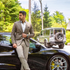 Man wearing a Broderick's Clothing Co. Au Noir EAMES brown blazer, white shirt, and beige trousers by a black sports car.