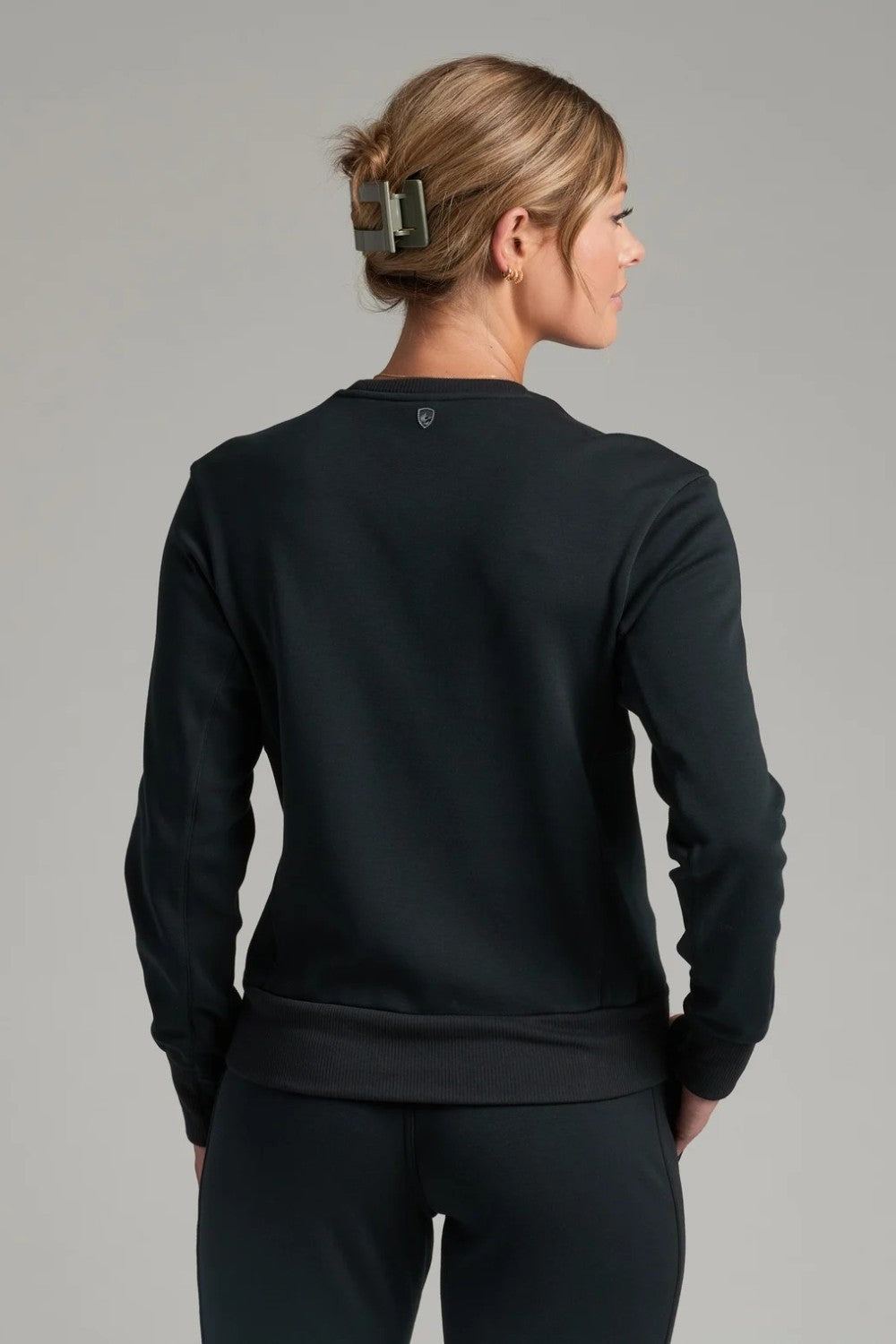 Back view of a woman wearing a black KÜHL Kozy Crew Sweatshirt from Broderick's Clothing Co. with ribbed hem details.