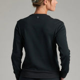 Back view of a woman wearing a black KÜHL Kozy Crew Sweatshirt from Broderick's Clothing Co. with ribbed hem details.
