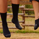 Broderick's Clothing Co. Smartwool black Merino wool crew socks worn by two people sitting on a wooden fence outdoors.