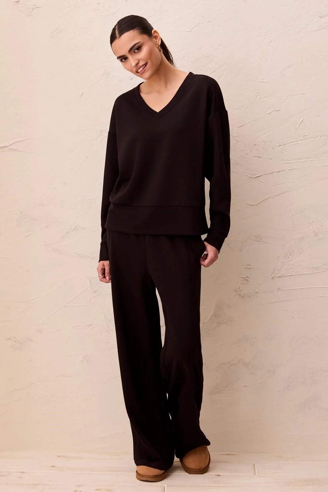 Model wearing Broderick's Clothing Co. black V-neck drop shoulder pullover in smooth techno lux scuba knit fabric.