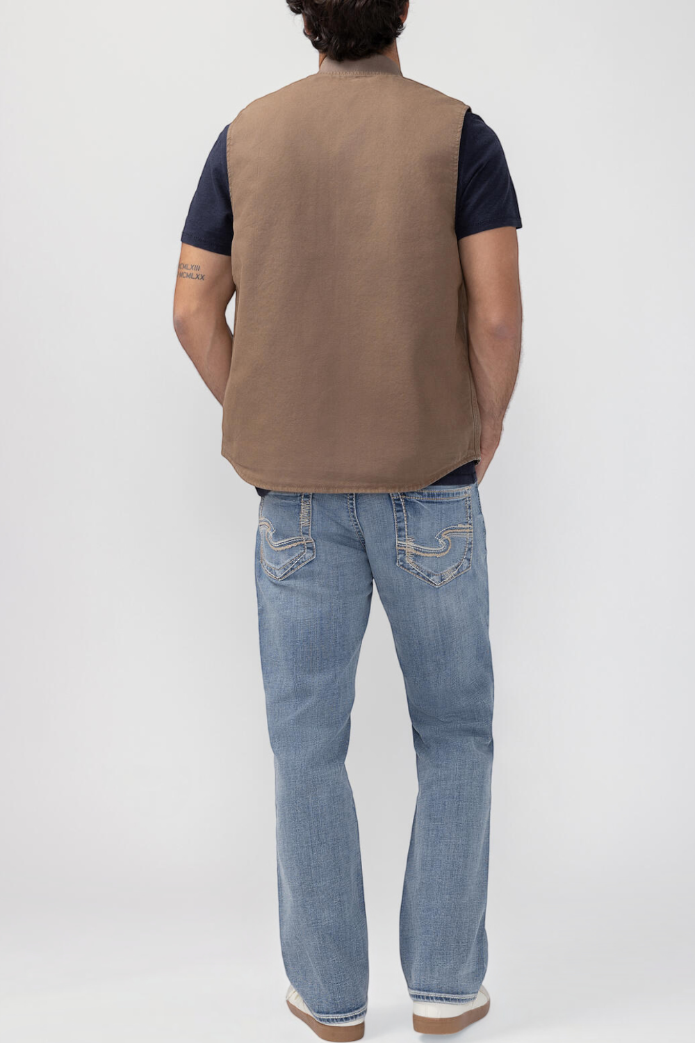 Broderick's Clothing Co. brown taupe workwear vest worn over a dark t-shirt and blue jeans, back view.