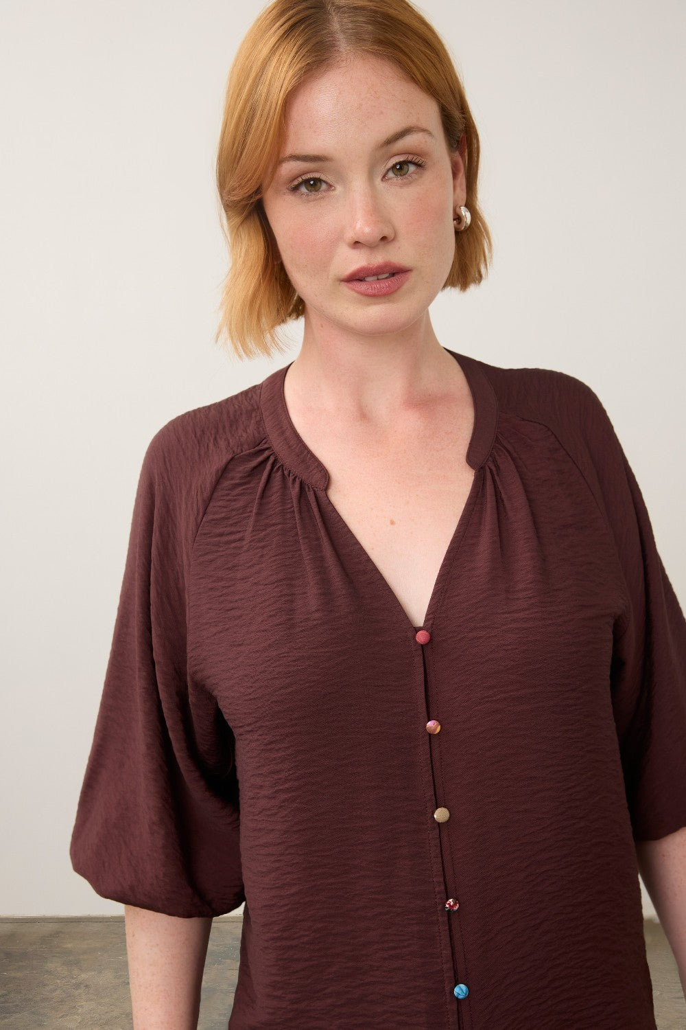 Broderick's Clothing Co. burgundy 3/4 sleeve blouse with colourful buttons and a V-neckline worn by a woman