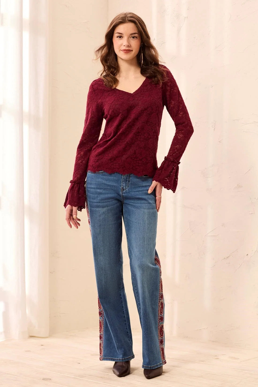 Broderick's Clothing Co. burgundy lace top with V-neck, scalloped hem, and flared cuffs worn with patterned jeans.