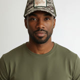 Broderick's Clothing Co. Goorin Bros. camo trucker hat with engraved bass patch worn by a man in an olive t-shirt.