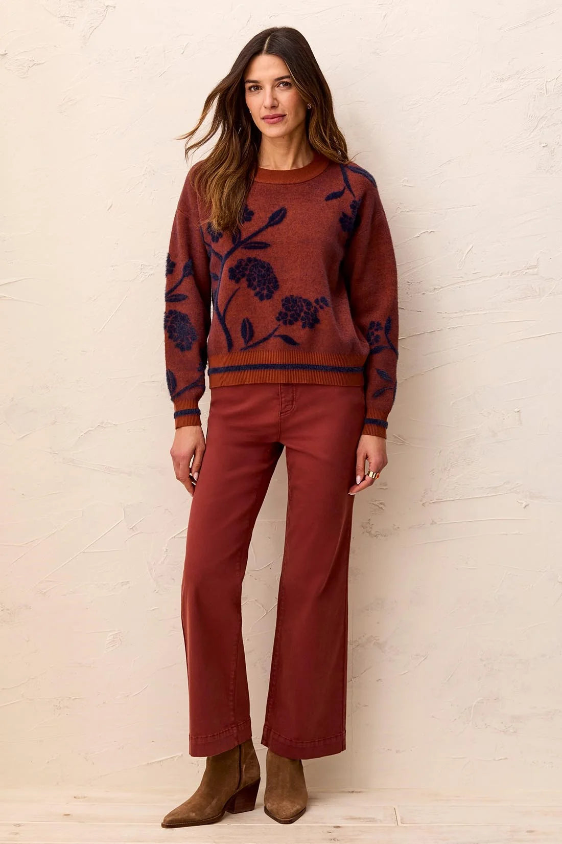 Model wearing a Broderick's Clothing Co. cedar mock neck sweater with navy floral embroidery and striped hem details.