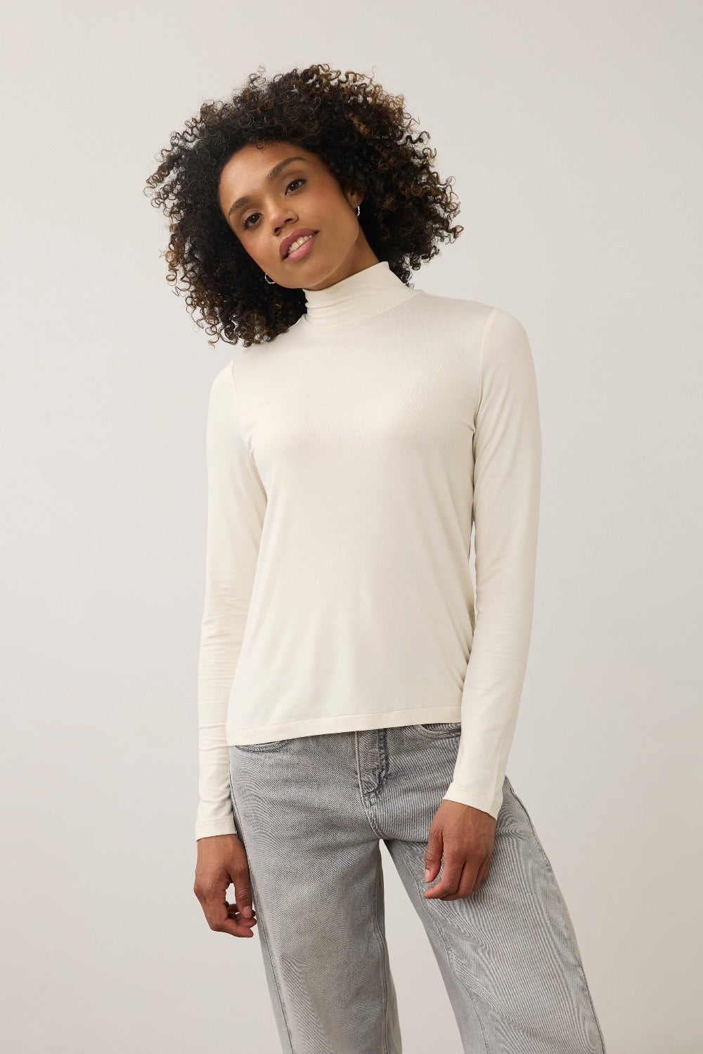 Broderick's Clothing Co. FDJ long sleeve cream mock neck top worn by a woman with curly hair against a plain background