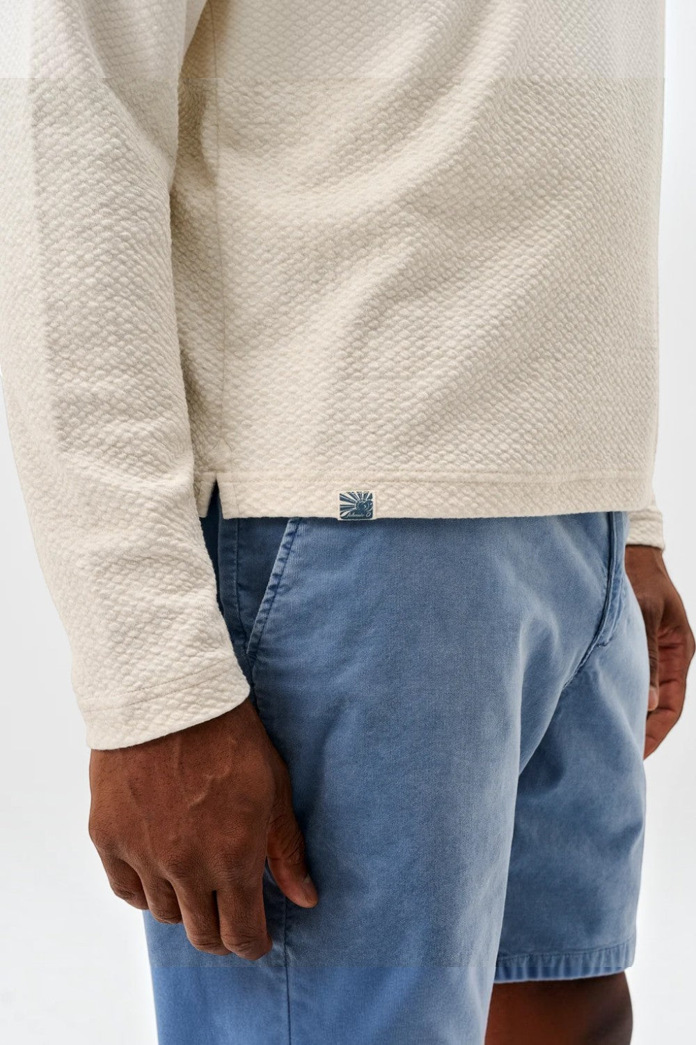 Broderick's Clothing Co. cream textured knit pullover with a hidden snap placket worn with blue shorts
