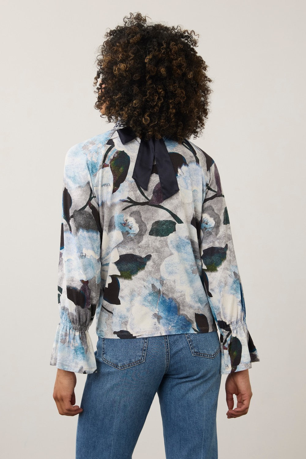 Broderick's Clothing Co. FDJ floral print long sleeve top with a navy blue bow tie back detail worn with blue jeans.