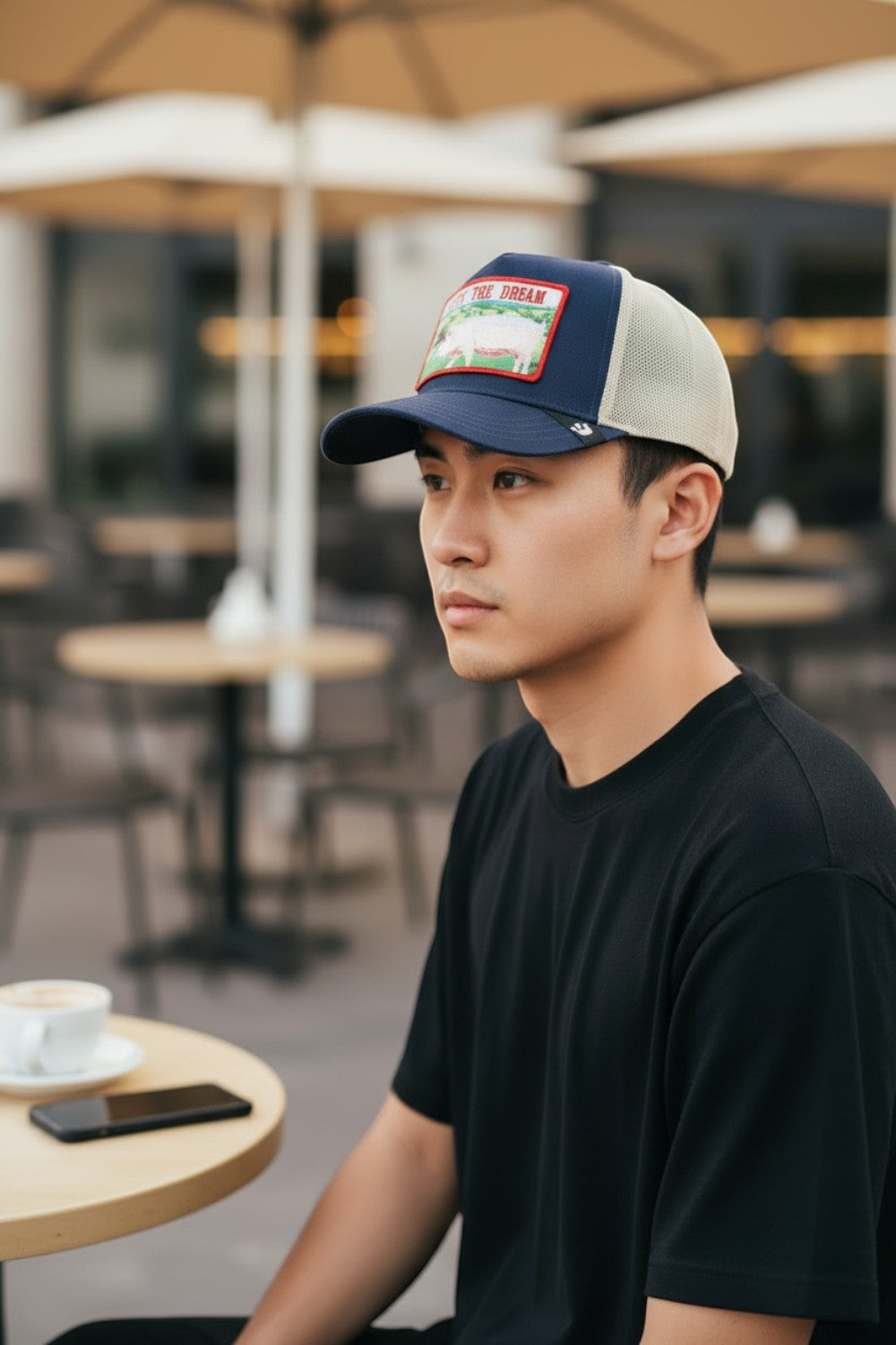 Man wearing a navy and beige Goorin Bros. LIVIN' THE DREAM trucker hat from Broderick's Clothing Co. at a cafe table.