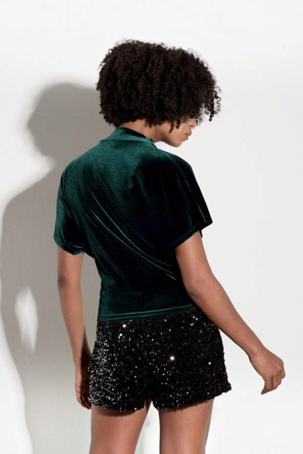 Model wearing a Broderick's Clothing Co. dark green velvet top with a high cowl neck and ruched side detail.