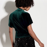 Model wearing a Broderick's Clothing Co. dark green velvet top with a high cowl neck and ruched side detail.