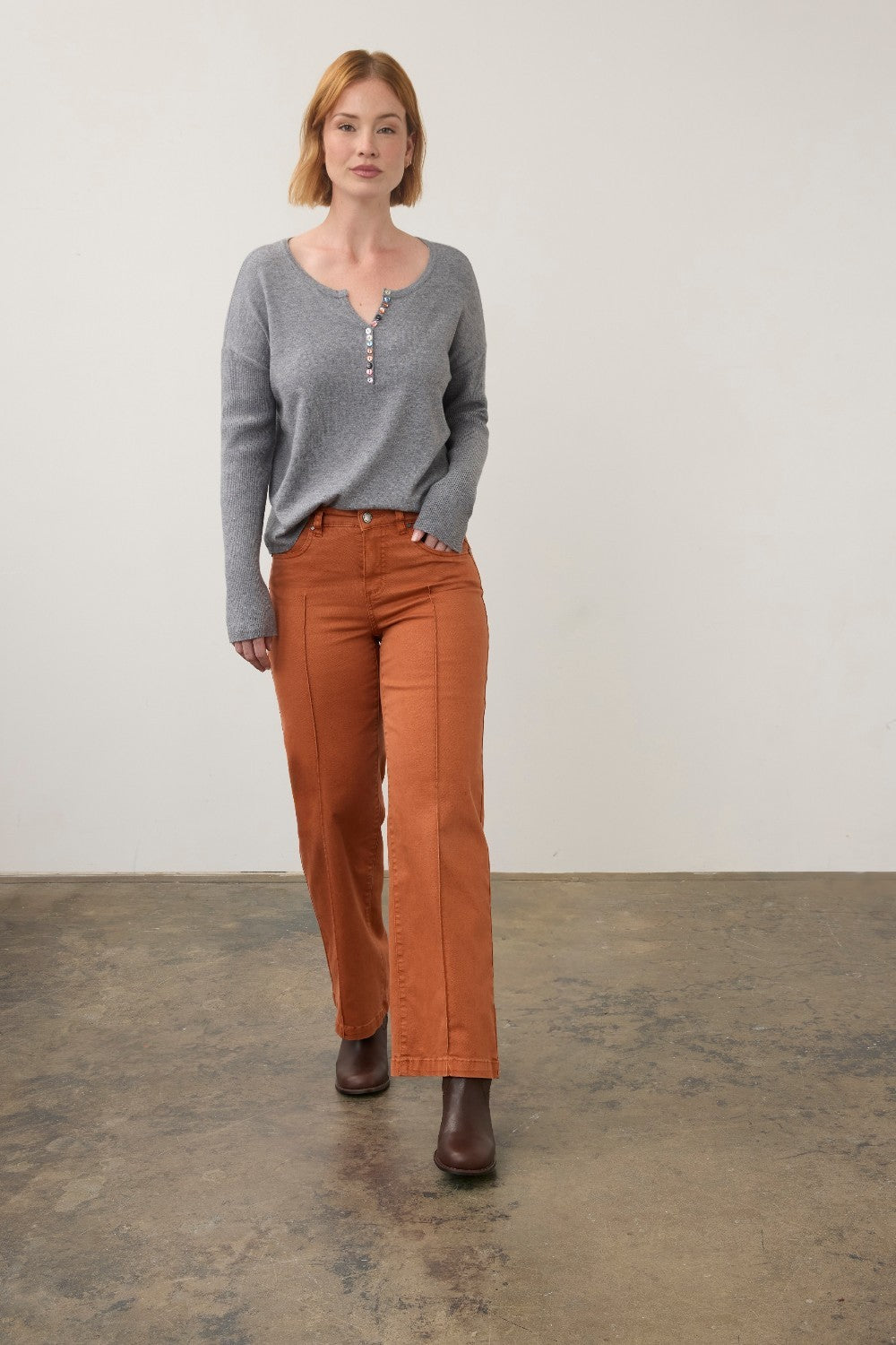 Broderick's Clothing Co. grey notch neck sweater with ribbed sleeves and colourful buttons paired with orange pants.