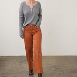 Broderick's Clothing Co. grey notch neck sweater with ribbed sleeves and colourful buttons paired with orange pants.