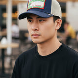 A man wearing a Broderick's Clothing Co. Goorin Bros. LIVIN' THE DREAM navy and beige mesh trucker hat.