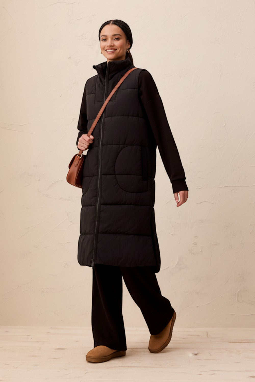 Broderick's Clothing Co. long black quilted vest with zip-front closure worn by a smiling woman in a studio setting.