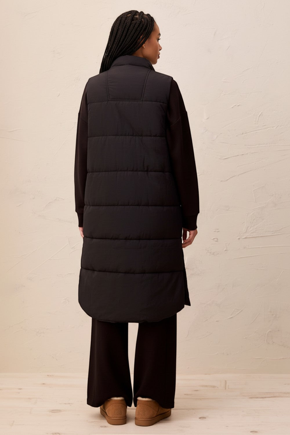 Back view of a model wearing a Broderick's Clothing Co. black longline quilted vest over a matching sweater.