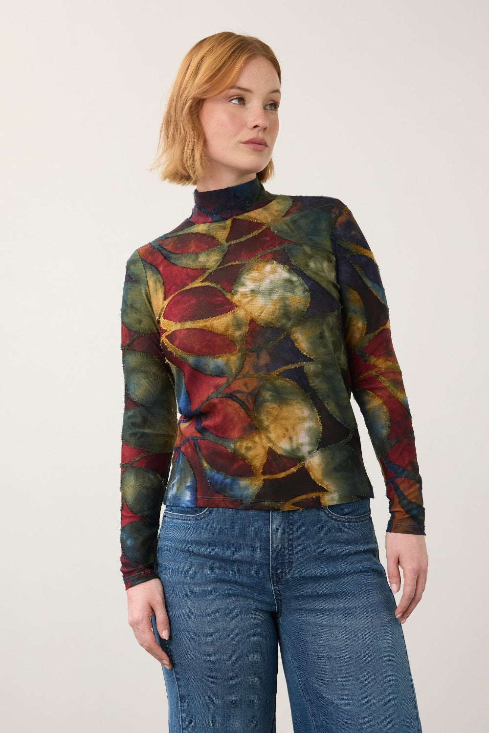 Broderick's Clothing Co. long sleeve mock neck top with a bold multi-colored leaf print worn with blue jeans.