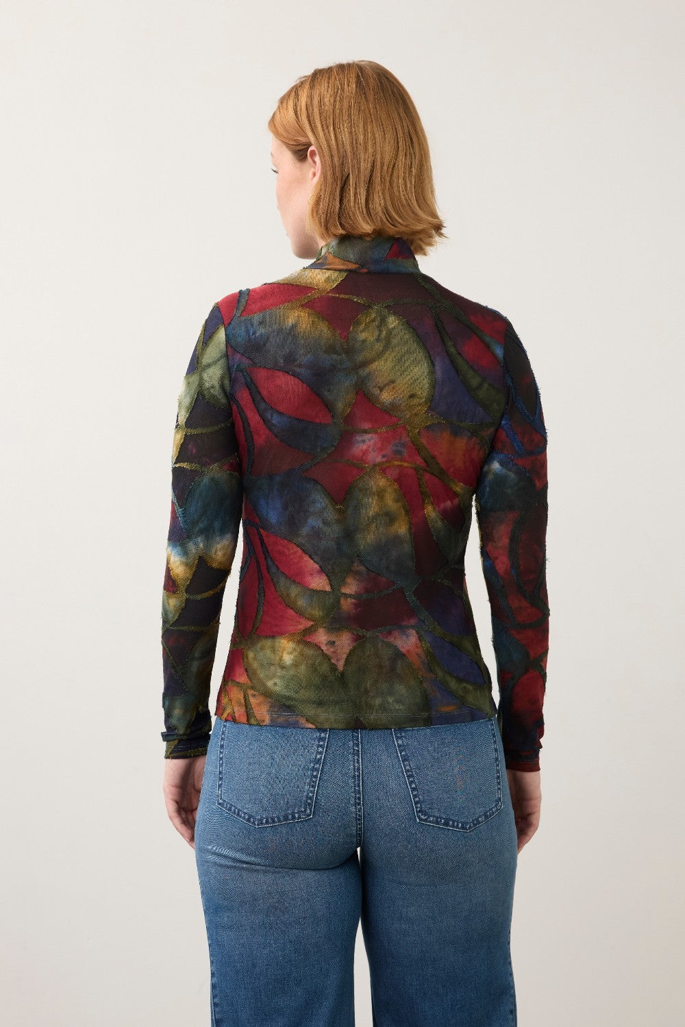 Broderick's Clothing Co. long sleeve mock neck top with a bold multicolored abstract print worn with blue jeans.